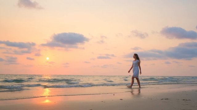 Young beautiful girl in a white dress walking along the beach. Ocean. 4k