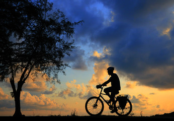 Obraz premium Silhouette man and bike relaxing on blurry sunrise sky background.