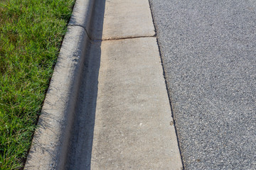 Generic formed concrete curb between green grass and asphalt street, horizontal aspect
