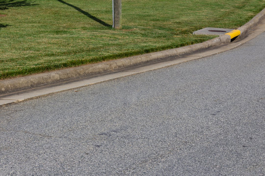Generic street and sweeping curb, green grass and yellow drain, horizontal aspect
