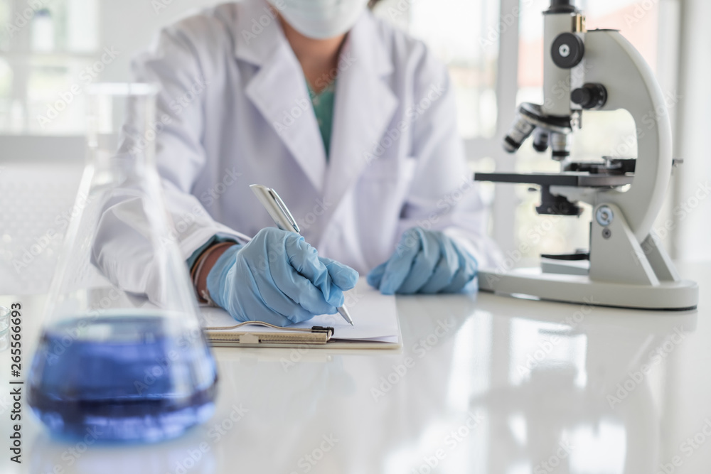 Wall mural a scientist hands writing on a clipboard in laboratory with test tube microscope and solutions.