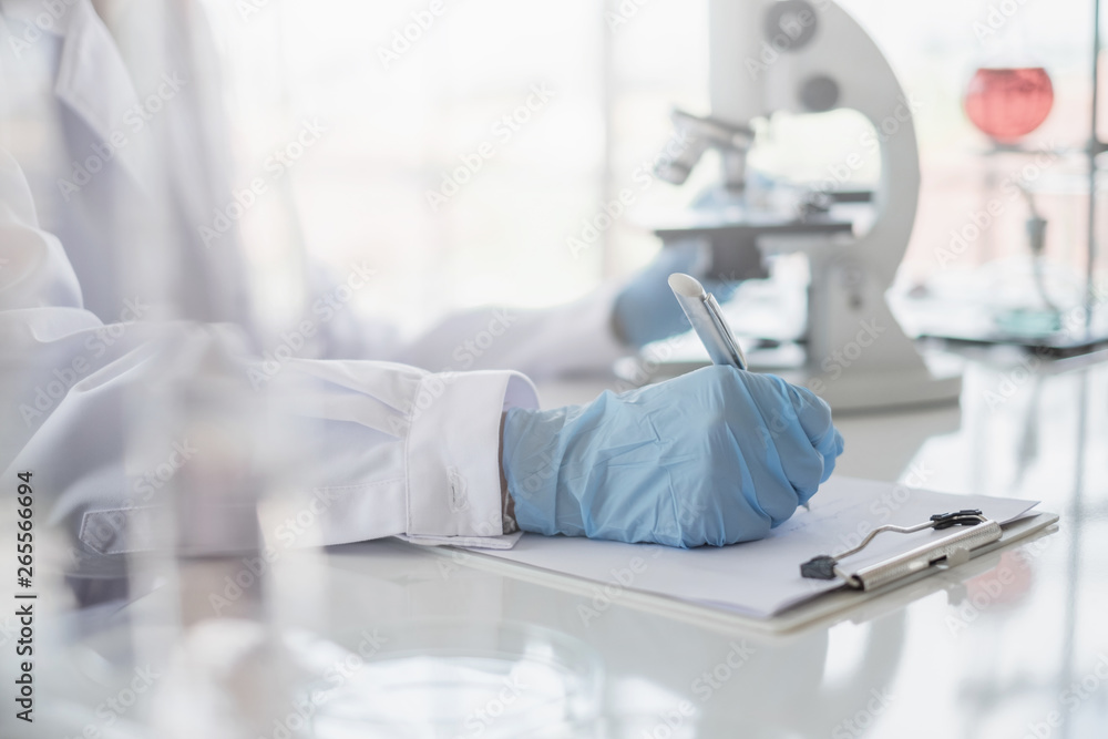 Wall mural a scientist hands writing on a clipboard in laboratory with test tube microscope and solutions.