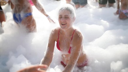 4k slow motion video of cheerful young woman in red bikini dancing on the beach covered in soap foam. Happy summer holiday and vacation