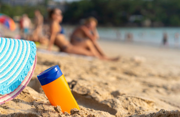 Summer Concept. Protective sunscreen or sunblock and sunbathe lotion in orange plastic bottles with colourful Straw hat on tropical beach, summer beach accessories in holiday, copy space for text you