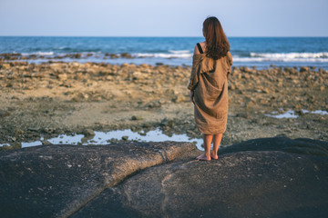 Rear view of a beautiful asian woman standing alone on the beach by the seashore