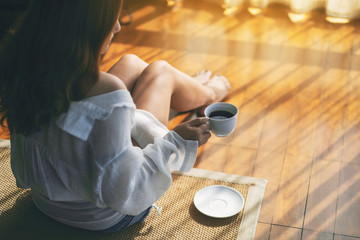 Top view image of a woman sitting and holding a cup of hot coffee on the floor in the morning