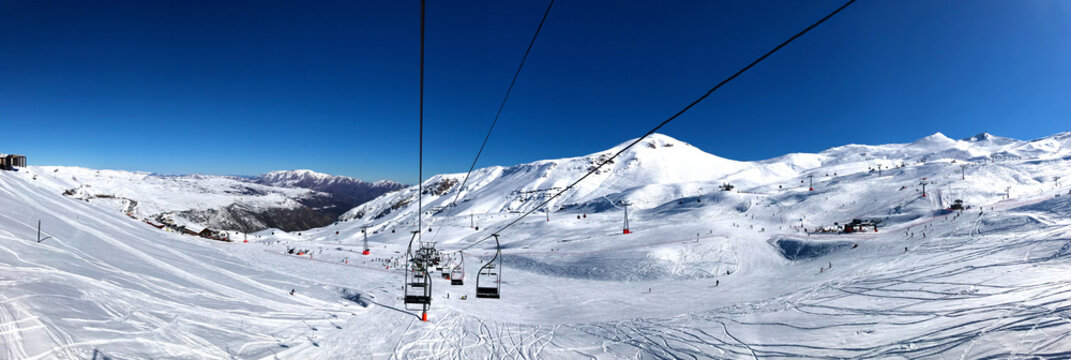 Panorama view of ski resort, slope, people on the ski lift, skiers on the piste among white snow in Valle Nevado near Santiago de Chile. Winter season extreme sports in South America.