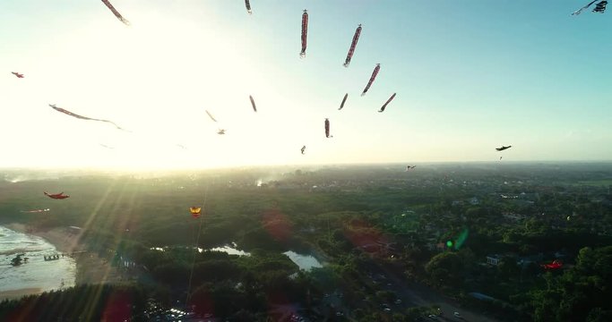 Aerial flies up shot many traditional Balinese kites flying in the air above seaside at sunset, Sanur, Bali, Indonesia. 4K