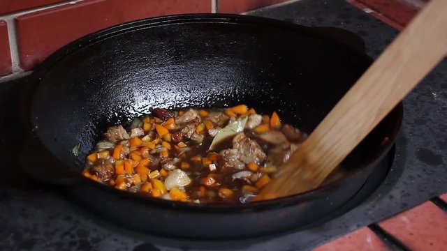 human hand added cumin spice in the boiling oil with meat and vegetables and mixing it, preparation of pilaf