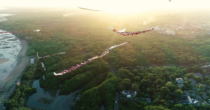 Aerial shot traditional Balinese kites flying in the air above seaside at sunset, Sanur, Bali, Indonesia. 4K