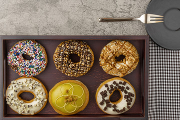 food background of assortment of donuts on wooden tray with napkin fork and small plate