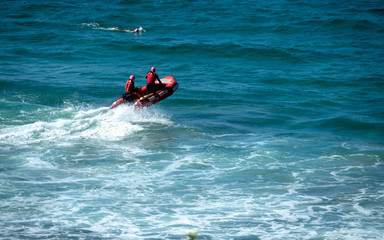 Beach rangers on a red rescue boat a surfer swimming nearby