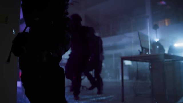 Masked Squad of Armed SWAT Police Officers Storm a Dark Seized Office Building with Desks and Computers. Soldier Breaks a Glass with His Arm and Team Continue to Move and Cover Surroundings.