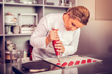 Concentrated female person squeezing dough on baking tray