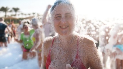 4k slow motion video of cheerful young woman in red bikini dancing on the beach covered in soap foam. Happy summer holiday and vacation