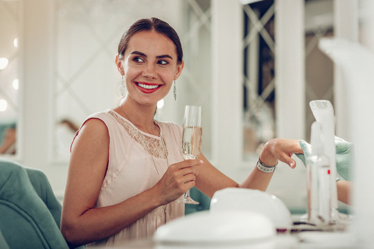 Appealing woman with tied hair being in great mood while drinking sparkling wine