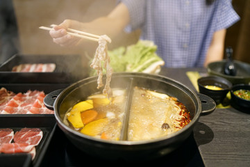 Holding sliced pork using chopsticks on hot pot with smoke for Japanese hot pot also known as Shabu Shabu or Sukiyaki is Japanese style.