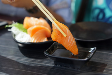 Salmon Sashimi - Hand holding chopsticks to pick fresh salmon and dip into soy sauce with wasabi, Japanese food style.