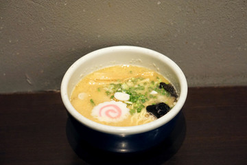 Shio Ramen - A bowl of Japanese noodles soup, topped with sliced braised pork (Chashu), black fungus and spring onions on wooden table.