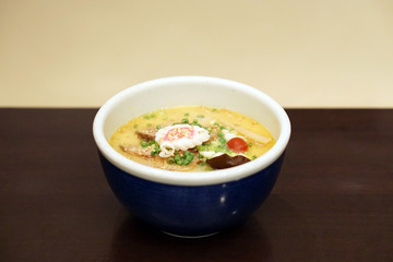 Tonkotsu Ramen - A bowl of Japanese noodles soup, topped with sliced braised pork (Chashu), black fungus, pickled plum and spring onions on wooden table.