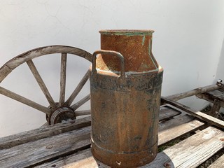 Carretilla antigua en madera para transportar mercancías y recipiente lechero de metal.