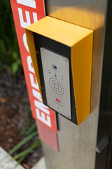 a close up photograph of an emergency button telephone intercom system on the side of a public path.