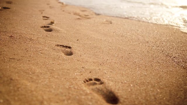 4k footage of footprints on golden beach sand at sunset light