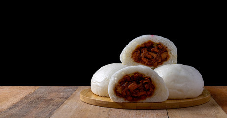 Steamed buns with red pork filling on a wooden tray and placed on a wooden table and a black...