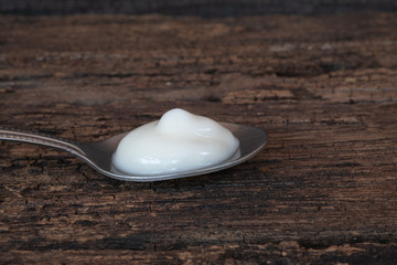 Natural homemade plain organic yogurt in spoon on wood texture background