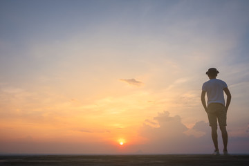 Fototapeta premium Traveler young man standing in the summer mountains at sunset and enjoying view of nature.