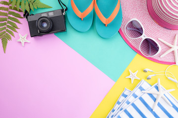 Beach accessories retro film camera, sunglasses, flip flop starfish beach hat and sea shell on pink and yellow background for summer holiday and vacation concept.