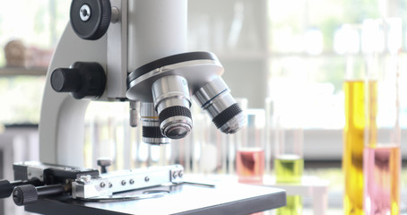 Close up of microscope in laboratory with  blurred background of glass test tube stack.