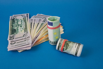 several wads of money of different currencies on a blue background.