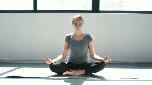 Young beautiful woman meditating during indoor training lotus pose Sporty girl doing yoga on the roof. Slow motion