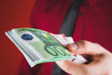 man in red suit holds out a wad of money in his hand on red background