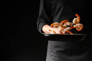 A professional cook prepares shrimps. Cooking seafood, healthy vegetarian food and food on a dark background. Horizontal view. Eastern kitchen