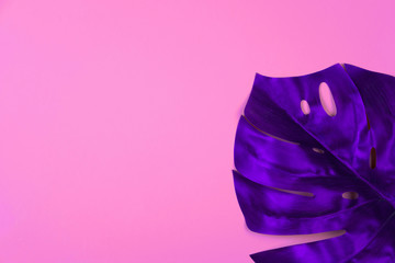 Vibrant bold purple tropical monstera leaf on pink background with copy space. Art neon surrealism concept