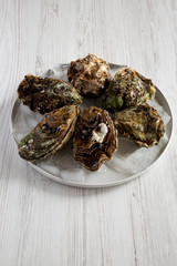 Fresh oysters on ice on a plate over white wooden surface, side view. Close up.