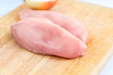 Raw Chicken Breasts, Fillets on a Wooden Cutting Board with Half Onion On White Background. Healthy Organic Food, Poultry Meat Cooking Concept. Copy space.