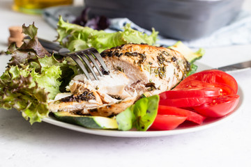 Baking chicken breast (fillet) with herbs and olive oil on a plate with green salad, tomatoes and grilled zucchini.