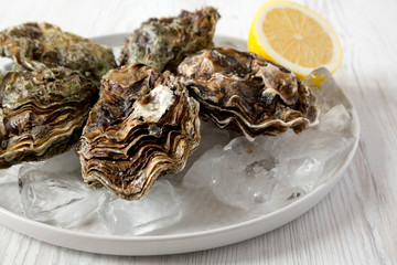 Fresh oysters on ice on a plate over white wooden surface, side view. Close-up.