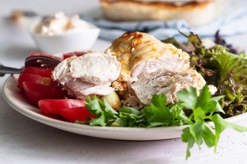 Baking chicken breast (fillet) with cream cheese sauce on a plate with green salad, tomatoes and grilled zucchini.