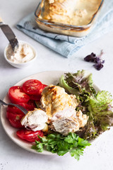 Baking chicken breast (fillet) with cream cheese sauce on a plate with green salad, tomatoes and grilled zucchini.