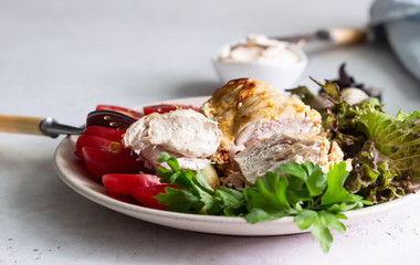 Baking chicken breast (fillet) with cream cheese sauce on a plate with green salad, tomatoes and grilled zucchini.