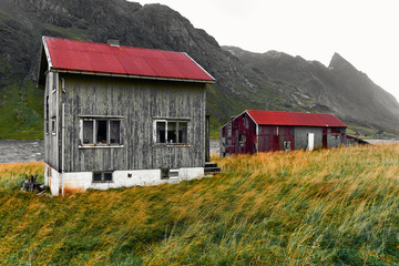 Fototapeta na wymiar Old damaged wooden house and barn with a red corrugated iron rooftop in the village Vinstad on Lofoten Islands in Norway.