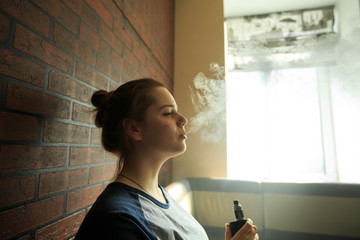 Vape teenager with  problem skin. Portrait of young cute girl smoking an electronic cigarette in the bar. Bad habit that is harmful to health. Vaping activity.