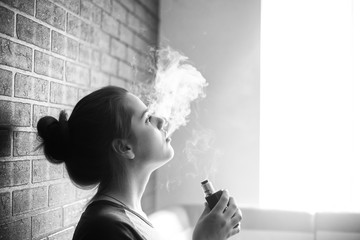 Vape teenager with  problem skin. Portrait of young cute girl smoking an electronic cigarette in the bar. Bad habit that is harmful to health. Vaping activity. Black nad white.