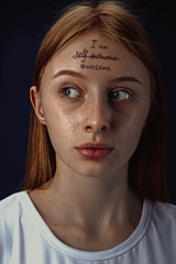 Portrait of young woman with mental health problems. The image of a tattoo on the forehead with the words I'm self-destructed-awesome. Concept of hidding the true feelings, psycological trouble.
