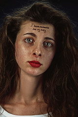 Portrait of young woman with mental health problems. Tattoo on the forehead with the words I have anorexia-love my body. Concept of hidding the true feelings, psycological trouble, treatment.