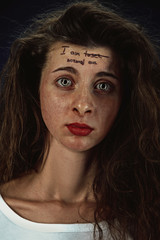 Portrait of young woman with mental health problems. The image of tattoo on the forehead with the words I am loser-normal one. Concept of hidding the true feelings, psycological trouble, treatment.